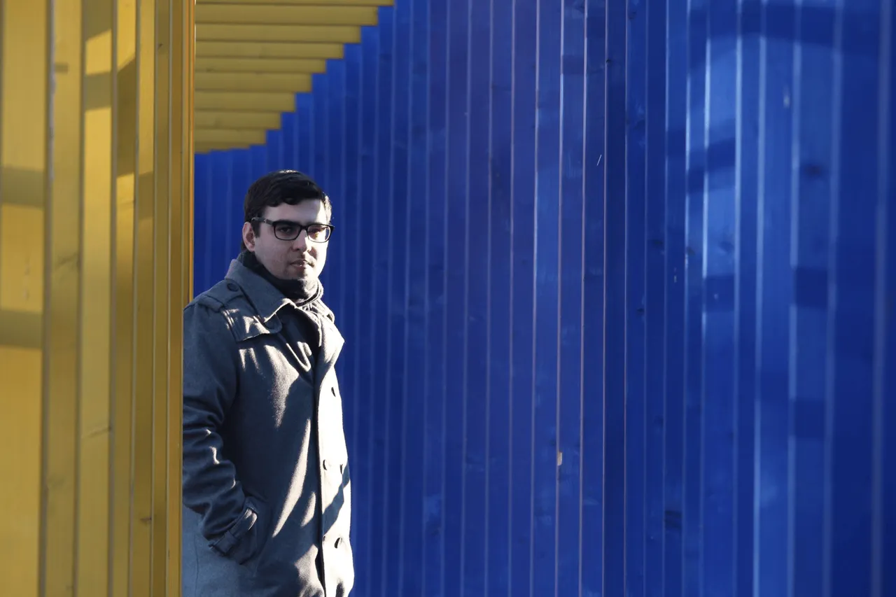 Eladio Aguilar in a grey coat against a blue and yellow slatted wall