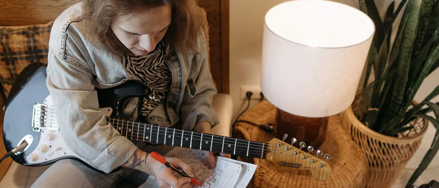 A songwriter writing on paper with an electric guitar